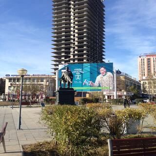 A man on a billboard seems to reach out towards a metal statue of a man in a chair.