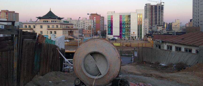 A concrete mixer stands on an empty section. In the distance the skyline is a mixture of traditional temples and garish high rises.