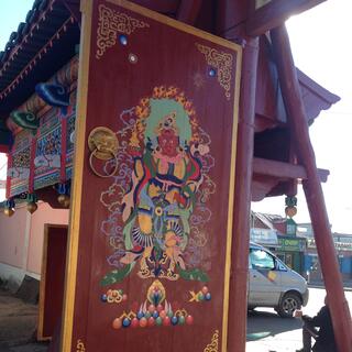 An ornate wooden painting of a dark skinned god wearing a pink scarf.