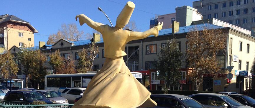 A cream statue of a dancing man wearing a long skirt and a tall hat.