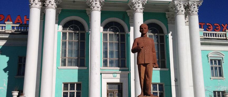 A bronze statue of a standing man wearing a dress jacket with a mandarin collar.