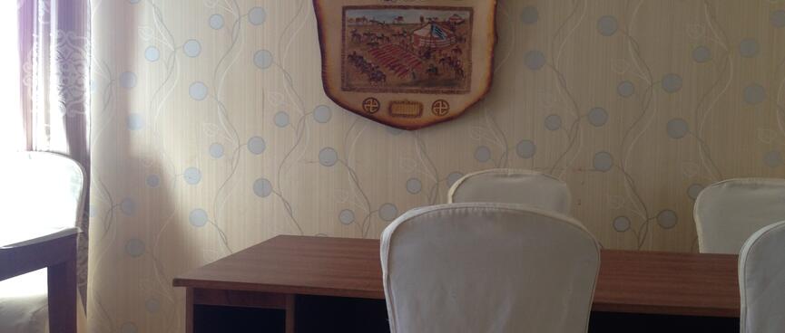 Neutral colour scheme, a wall hanging of Genghis Khan, white covered chairs and wooden tables.