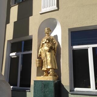 A golden statue of a woman in traditional Mongolian dress, carrying a lamb and a bucket.
