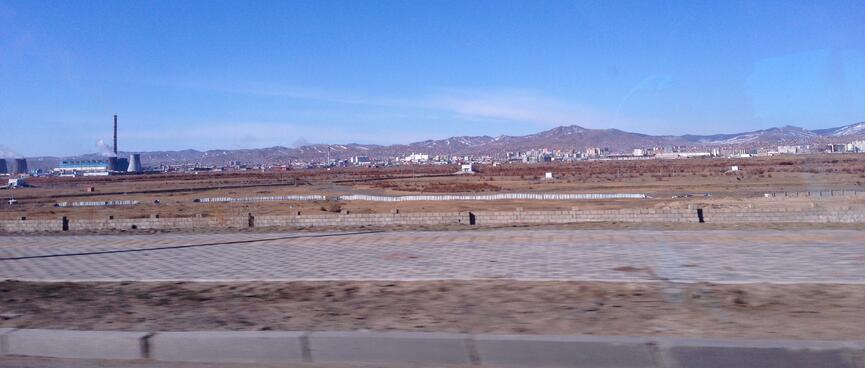 Empty steppes, a power plant and in the distance city buildings and low mountains.