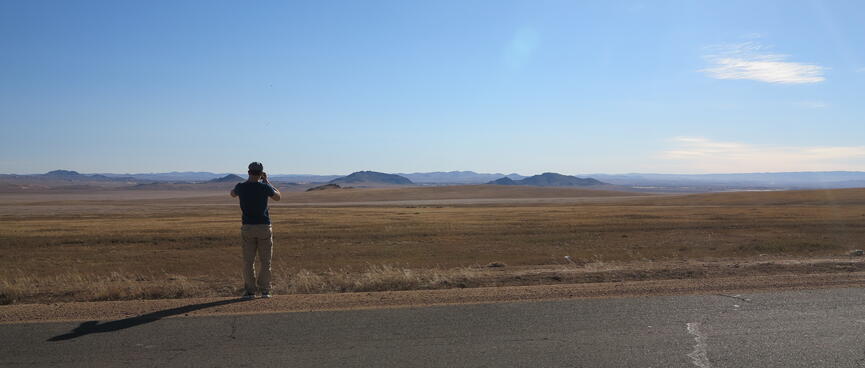 A man photographs steppes and distant hills.