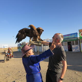 A lady in a blue cloak and brown hat waves her arms to scare the eagle.