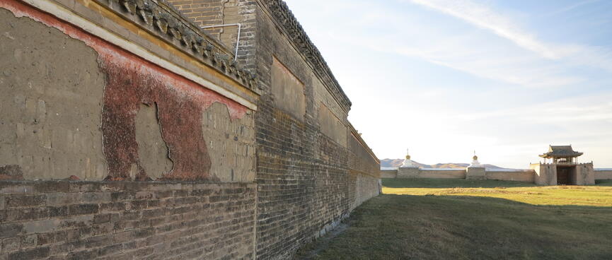 Remnants of red paint peel off a long brick wall.