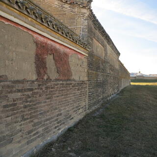 Remnants of red paint peel off a long brick wall.