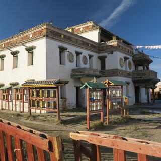 Prayer wheels and flags outside a two story stone building.