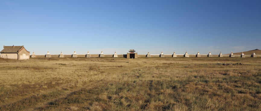 A long wall on the far side of a grassy field.