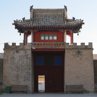 A small red building sits on top of a tall stone battlement containing a doorway.