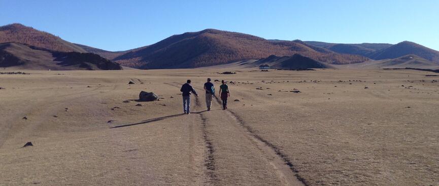 Three people walk towards the hills, following tyre tracks in the grass.
