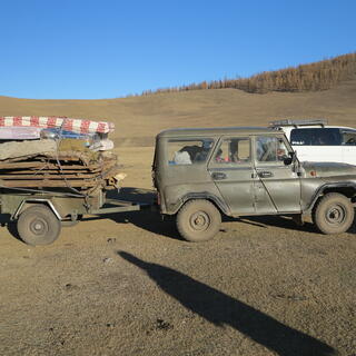 A green army jeep tows a small trailer stacked with belongings.
