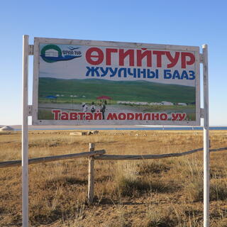 A billboard in a paddock shows white gers on a backdrop of green hills.