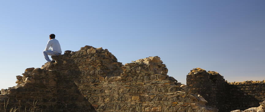 A man sits on top of derelict stone walls.