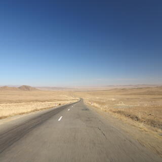 A grey two lane highway stretches through a light brown landscape.