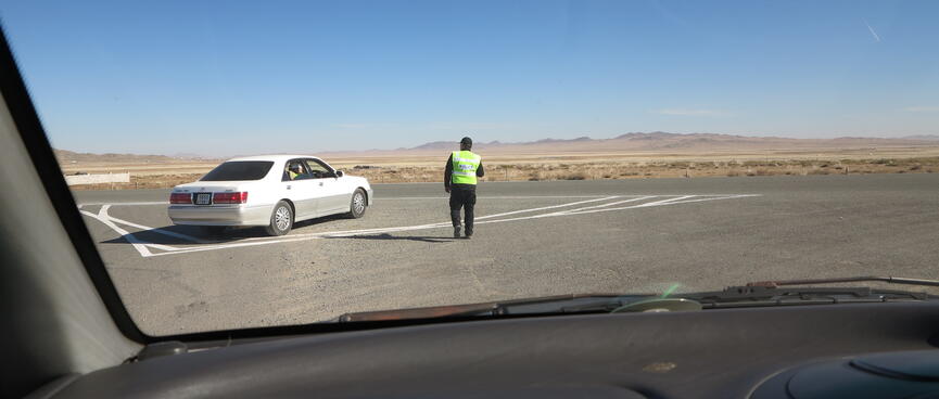 A man in a yellow vest approaches a parked car.