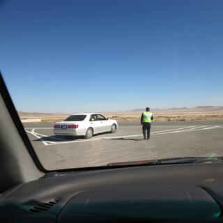 A man in a yellow vest approaches a parked car.
