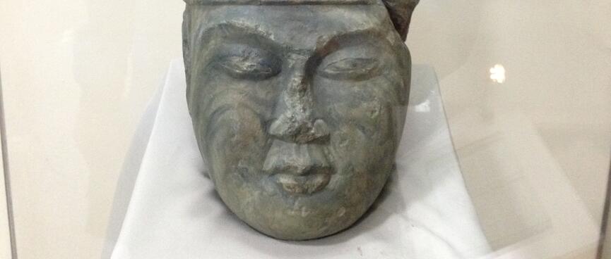 Carved stone head with closed eyes wearing a tall ceremonial headdress.
