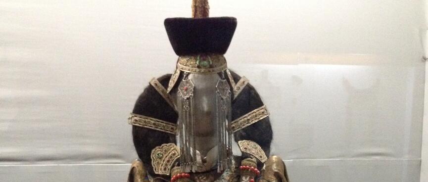 A mannequin in gold and red ceremonial robes has her hair tied in a loop.