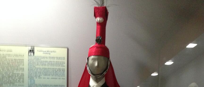 A mannequin wears a ceremonial cloak and a matching hat with a tall narrow extension.