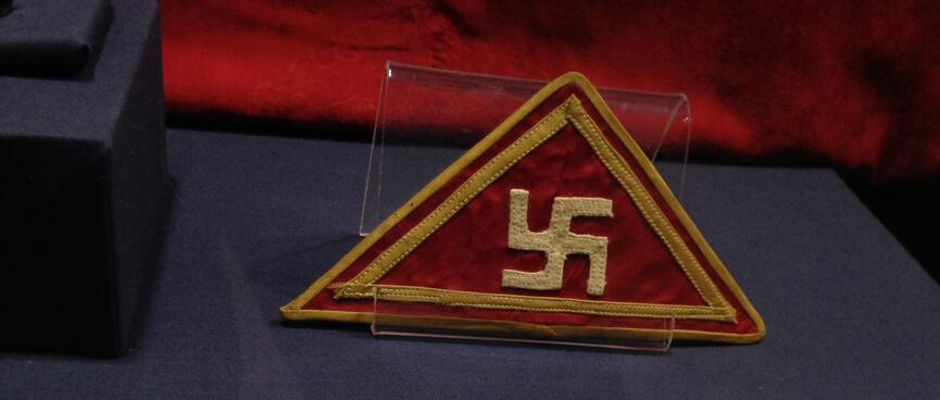 A sewn triangle badge with a gold swastika and border.