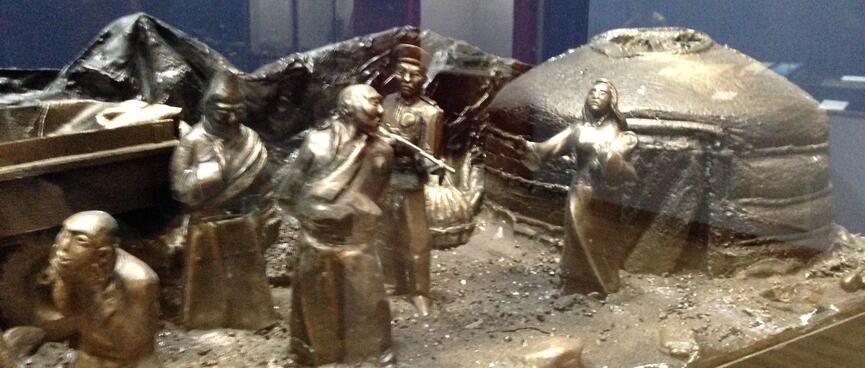 Metal sculpture of a woman at the doorway of a ger reaching her hand out to a man who is being escorted away by a soldier.