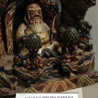 A shiny painted wooden statue showing a fat man with a white beard sitting in a doorway.