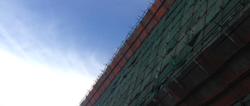 The side of a building is wrapped in green and red mesh.