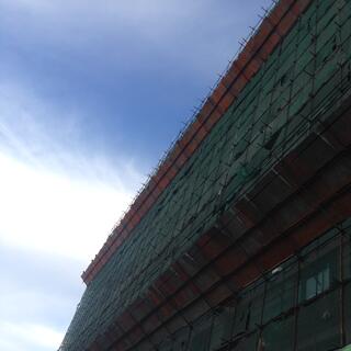 The side of a building is wrapped in green and red mesh.