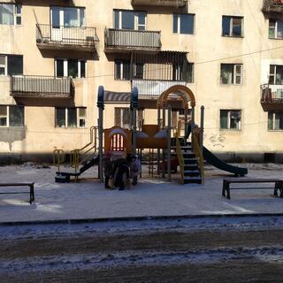 A parent clears snow off a playground slide while two children wait.