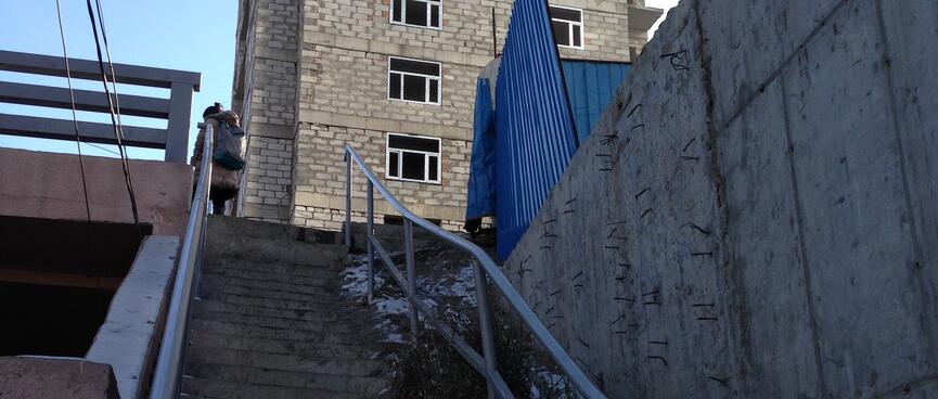 A steep staircase with a buckled rail takes a woman to a patched brick building.