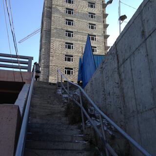 A steep staircase with a buckled rail takes a woman to a patched brick building.