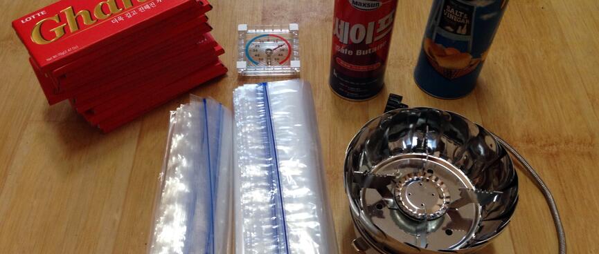 A fold up gas burner and cartridge, chocolate, chips and plastic bags.