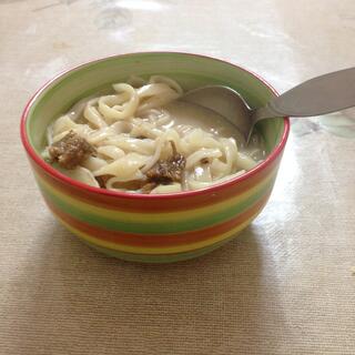 A striped bowl containing wide noodles and small meatballs.