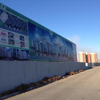 A large billboard for a new housing development depicts a concentrated cluster of tall apartment blocks.