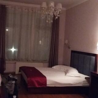 A pinky hued room containing a white bed with a red runner, and a fancy chandelier.