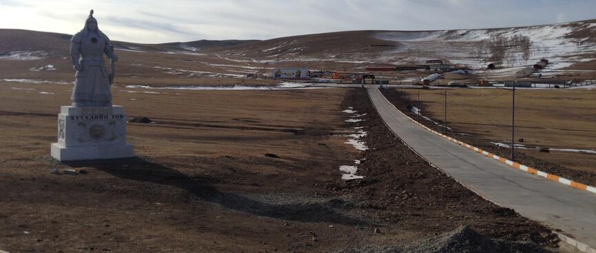 A statue of Genghis Khan next to a thin ashphalt road.