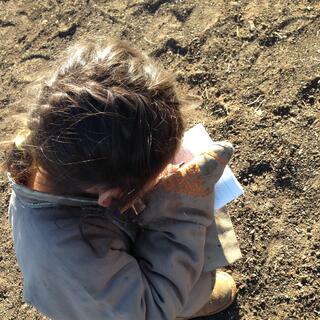 A little girl crouches and studies a notebook.