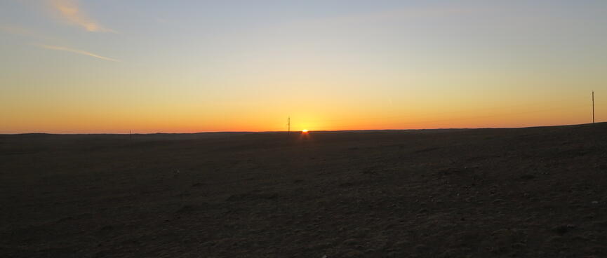 Light blue-orange sky and pinpoint of light at the black horizon.