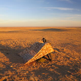 A wedge shaped canvas shelter covered in a repeating brown and yellow pattern.