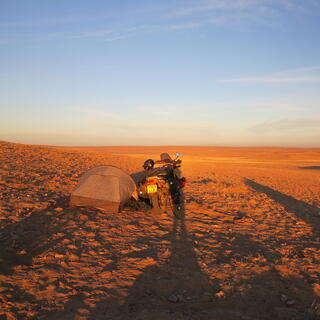 Tall shadows either side of a tent and a motorbike.