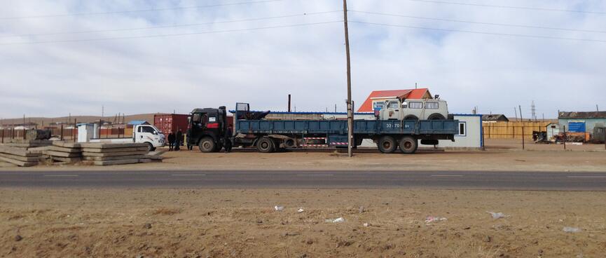 A long blue truck with a white Russian van on the back.