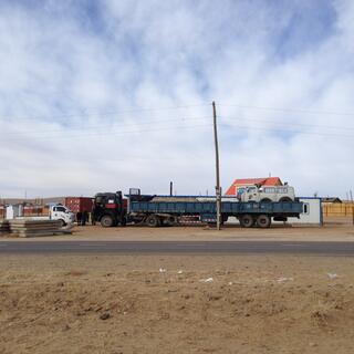 A long blue truck with a white Russian van on the back.