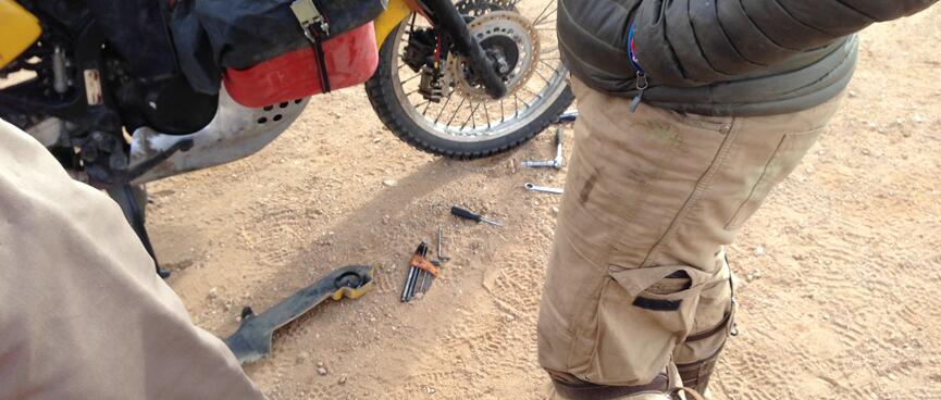 A partial view of legs, wheels and spanners lying in the sand.