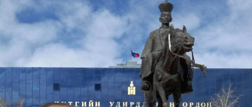 A statue of a horse rider has what looks like a chess pawn on his tall hat.