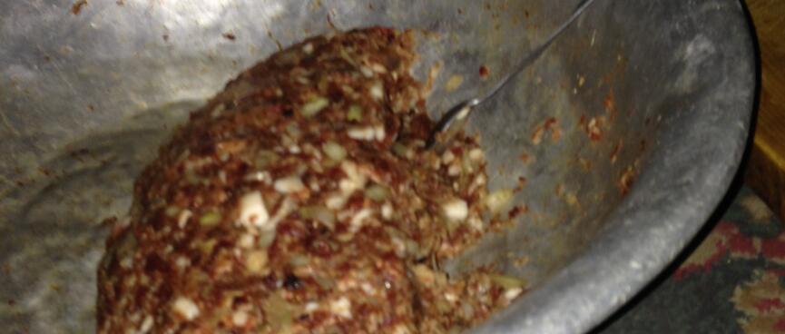 A metal bowl containing mashed meat with flecks of white and green.
