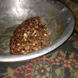 A metal bowl containing mashed meat with flecks of white and green.
