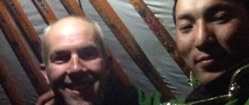 Photo with one of the brothers. He is wearing a long green coat and behind us are the patterned slats of the ger roof.