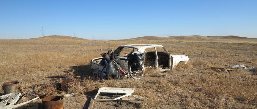 My bike leans against the back of a derelict car.